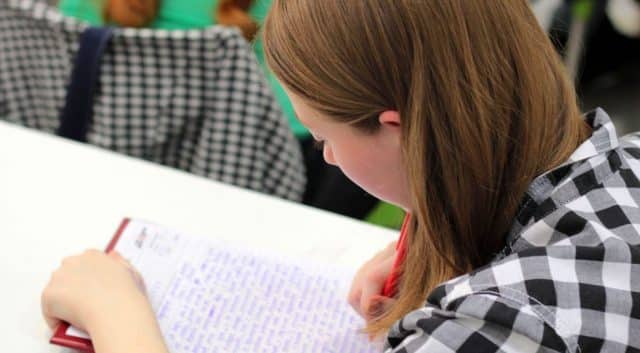 A young Autistic student is handwriting an exam in a separate room to other students. This is an example of Special Assessment Conditions in action.