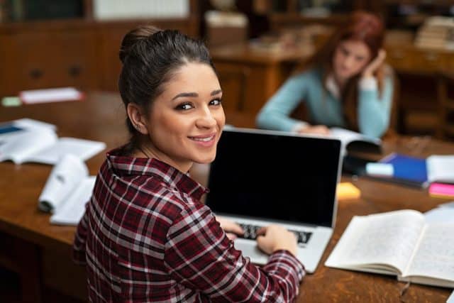 A decorative stock image showing a happy young woman working on a laptop and smiling at the camera.