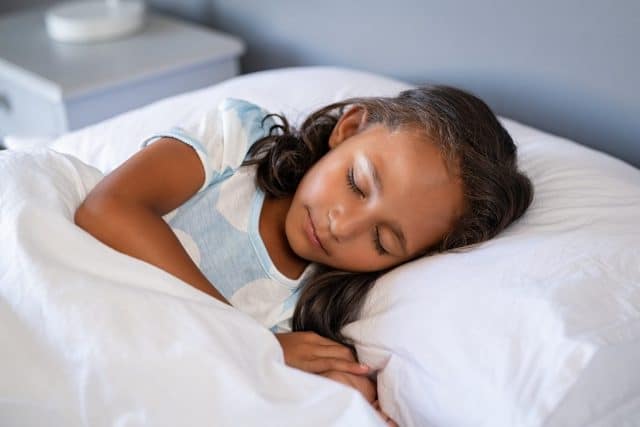 Stock image shows a little girl asleep in bed.