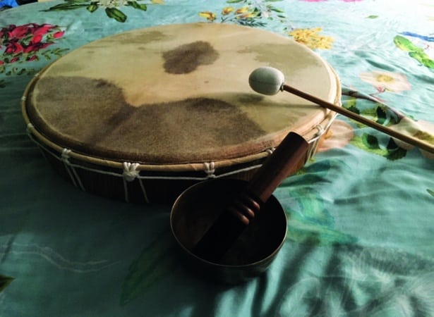 A shamanic drum rests on the table. A drumstick rests on the drum. 