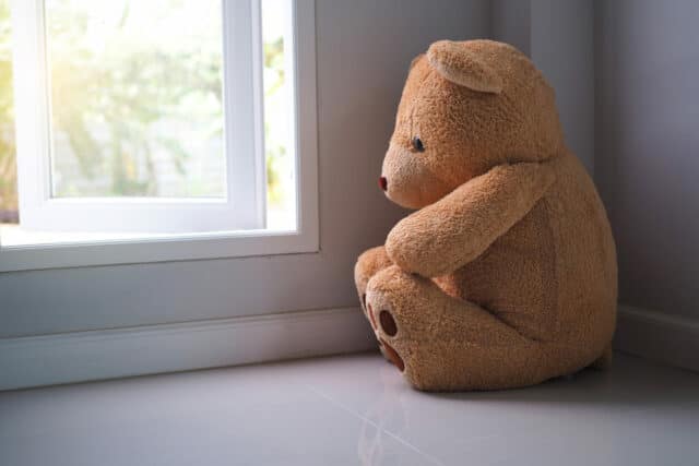 Teddy bear sitting looking out the house window alone. It seems sad.