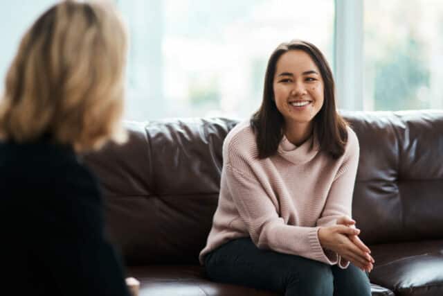 A woman is sitting on a couch, speaking to a therapist.